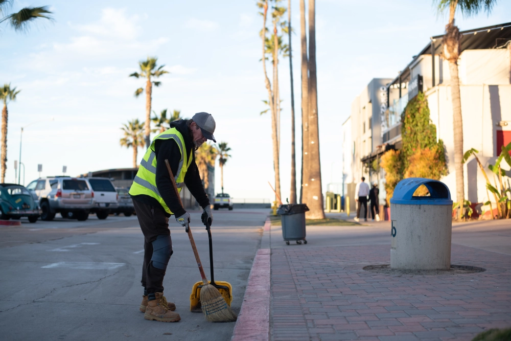 image of man sweeping up trash in Pacific Beach as part of the Community Care Crew